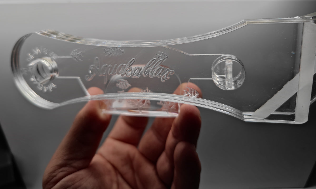Transparenter Aquakallax Algenschaber in der Hand mit eingraviertem Logo, Fischmotiven und zwei runden Grifföffnungen