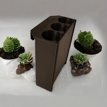 Schwarzer Aquakallax Aquaponic Hang-On Pflanzenträger mit drei runden Pflanzöffnungen in schräger Ansicht zwischen kleinen Pflanzen