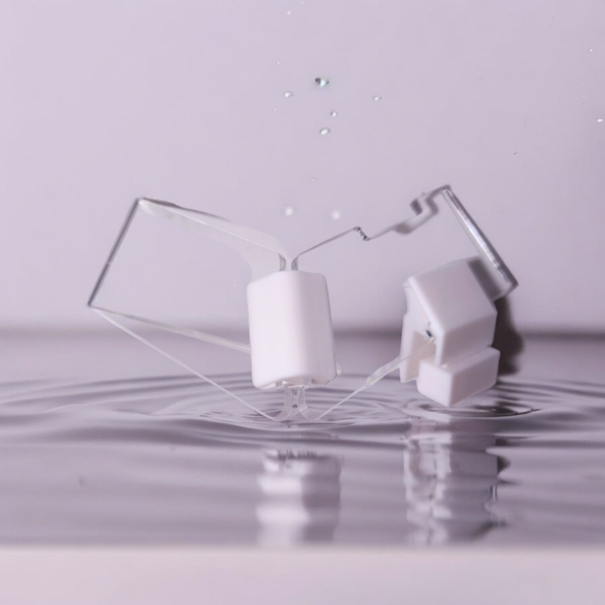 Zwei transparente Aquakallax JumpStop Sprungschutzecken mit weißen Klemmhaltern vor Wasserhintergrund