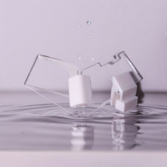 Zwei transparente Aquakallax JumpStop Sprungschutzecken mit weißen Klemmhaltern vor Wasserhintergrund