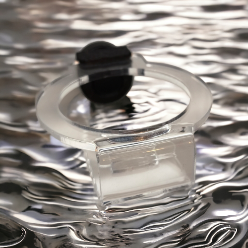 Transparenter Aquakallax Oxi-Hover-Haltering mit schwarzem Magnethalter in schräger Draufsicht vor einer Wasserkulisse