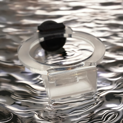 Transparenter Aquakallax Oxi-Hover-Haltering mit schwarzem Magnethalter in schräger Draufsicht vor einer Wasserkulisse